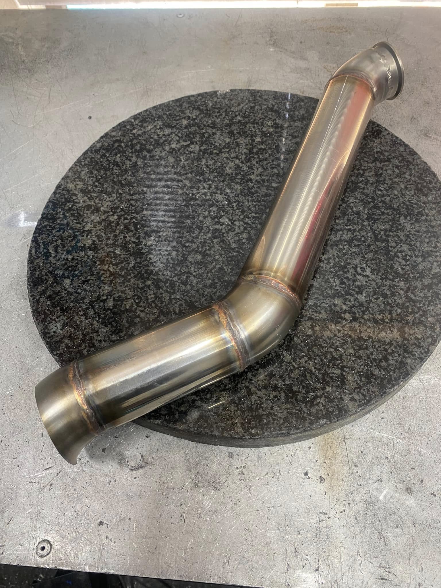 Custom welded boost pipe with bends and formed ends on the workshop bench.